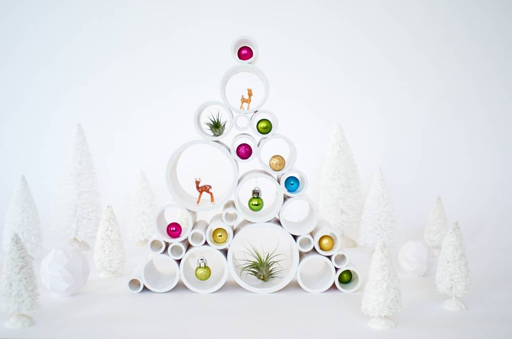 A stack of open round white piping, each one filled with a colored christmas ornament is surround by small white plastic Christmas trees.