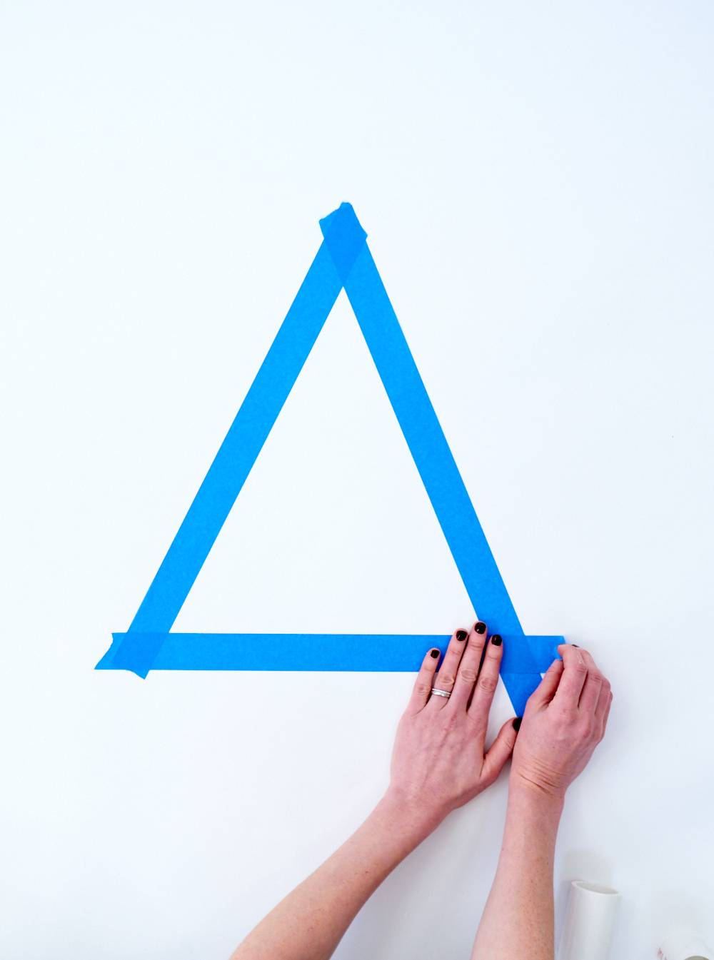 Hands placing blue tape to form a triangle on a white surface