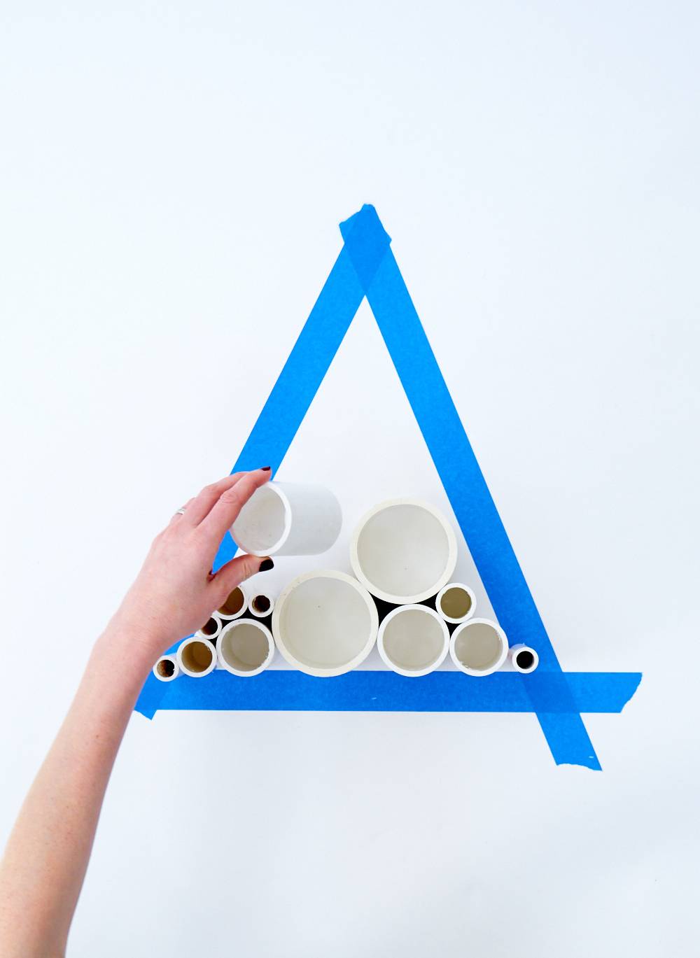 A person lines round pieces of PVC pipe up to fill a triangle space marked out blue tape.