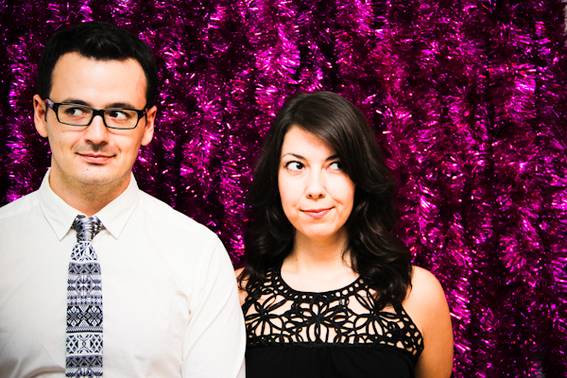 A dark haired man and a dark haired woman standing next to each other looking away from each other with their eyes.