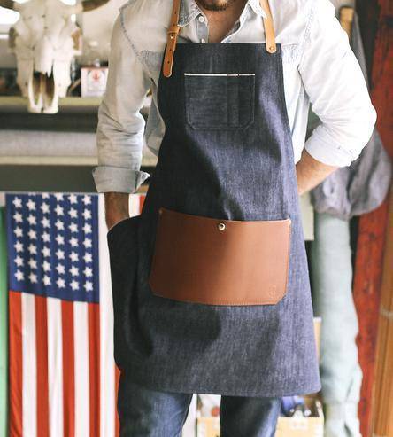 A person wears a denim apron near a flag.
