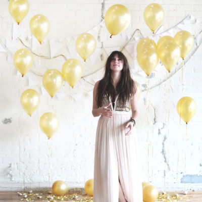 Woman posing for photo with gold colored balloons on the white background.