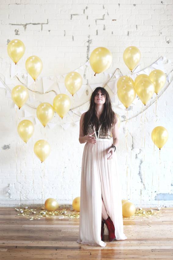 A woman in a white dress stands in front of a backdrop consisting of yellow party balloons.