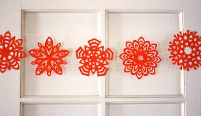 Red colored paper snowflake is decorated in a row with a thread.