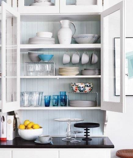 White kitchen cabinets organized to fit bowls and glasses of various dimensions.