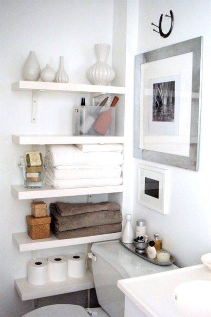 White bathroom with shelf filled with towels, tissue papers etc.