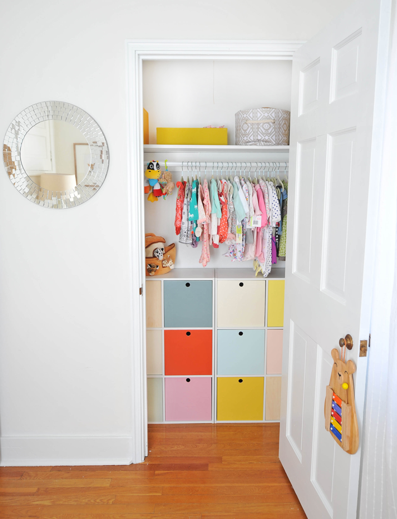 A closet is open to reveal colorful storage units and clothing.