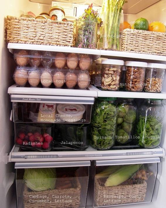 Refrigerator filled with fruits and vegetables stored in baskets and glass jars.
