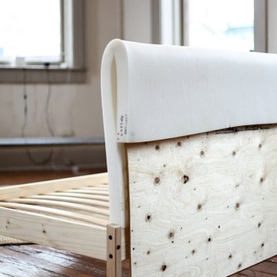 A slatted bed frame has cushioning thrown over a headboard above it.