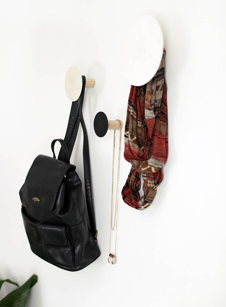 Black backpack and scarf hanging from wooden wall posts with round faces.