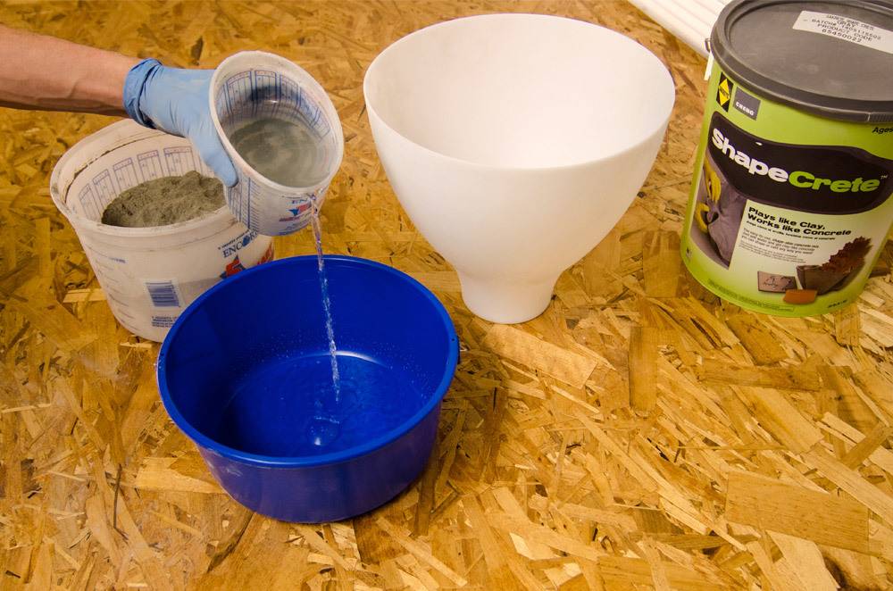 A gloved hand pouring water into a blue bowl on a scrap wooden floor.