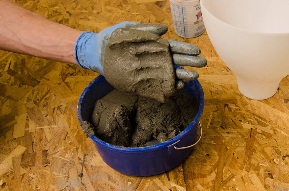 A hand is holding wet clay over a blue bucket.