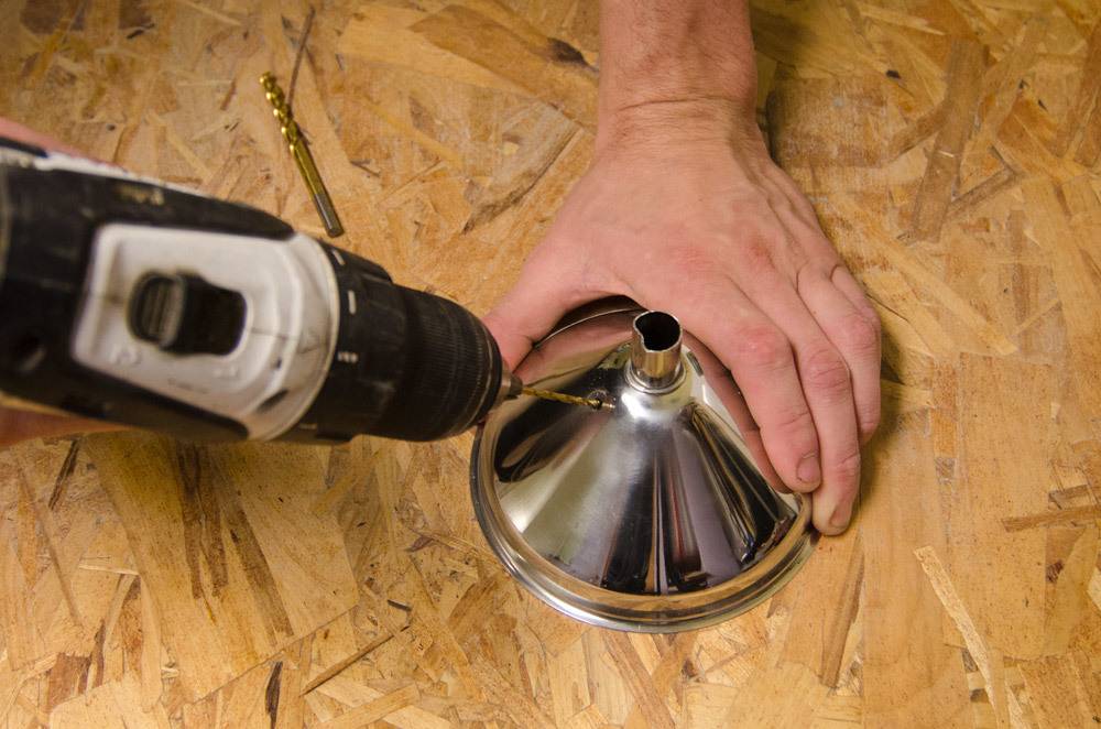 A person is drilling something into a metal funnel.