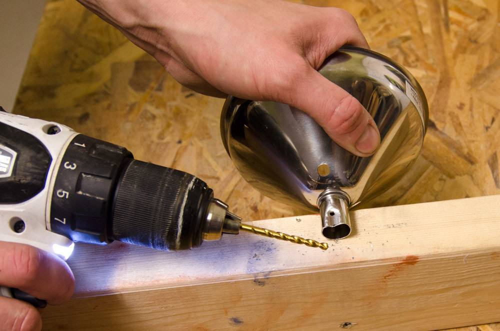 A person uses a drill on a piece of wood next to a metal funnel.
