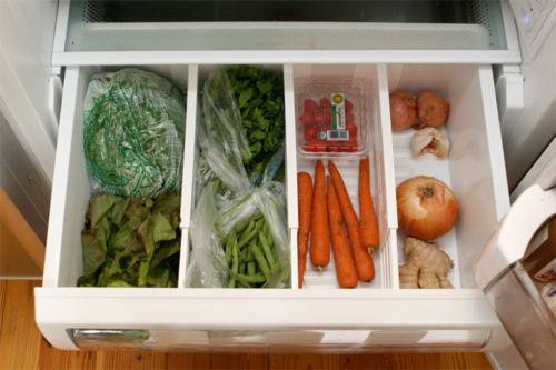 Vegetables are sorted into different areas of a fridge drawer.