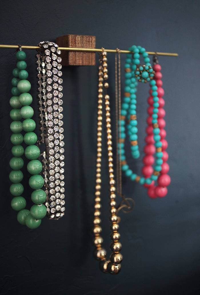 Wooden jewelry stand fixed on the wall holding a few necklaces of different colors.