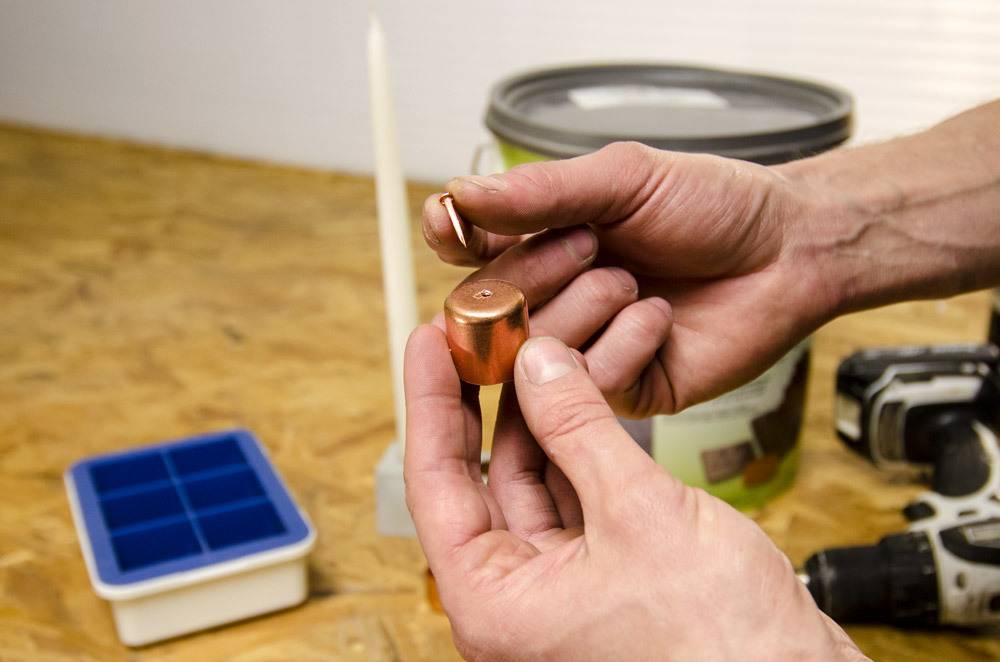 A person string to put a tiny copper nail into the top of a copper part with a drill and a can of paint in the background.