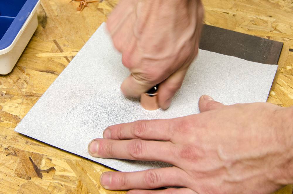 A man uses a stamp to drill a hole into paper on a plywood table.