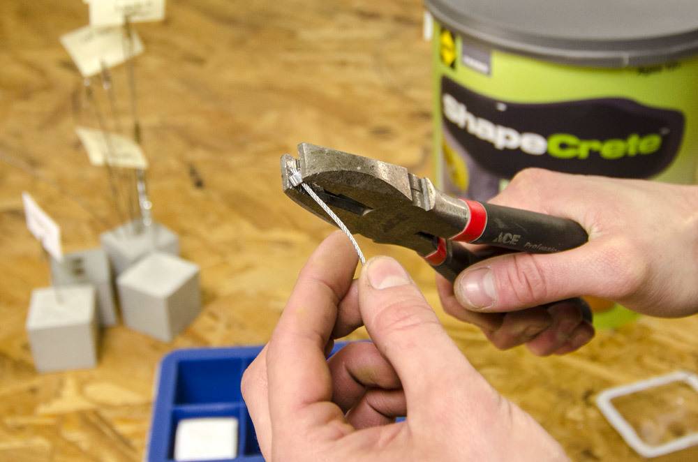 Man bending a small piece of metal with a pair of pliers over a wooden work bench.