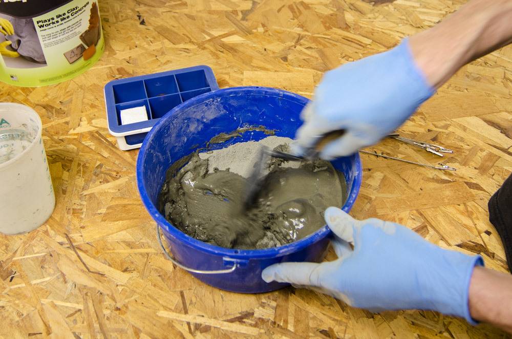 A person is wearing blue gloves as they mix cement in a blue container.