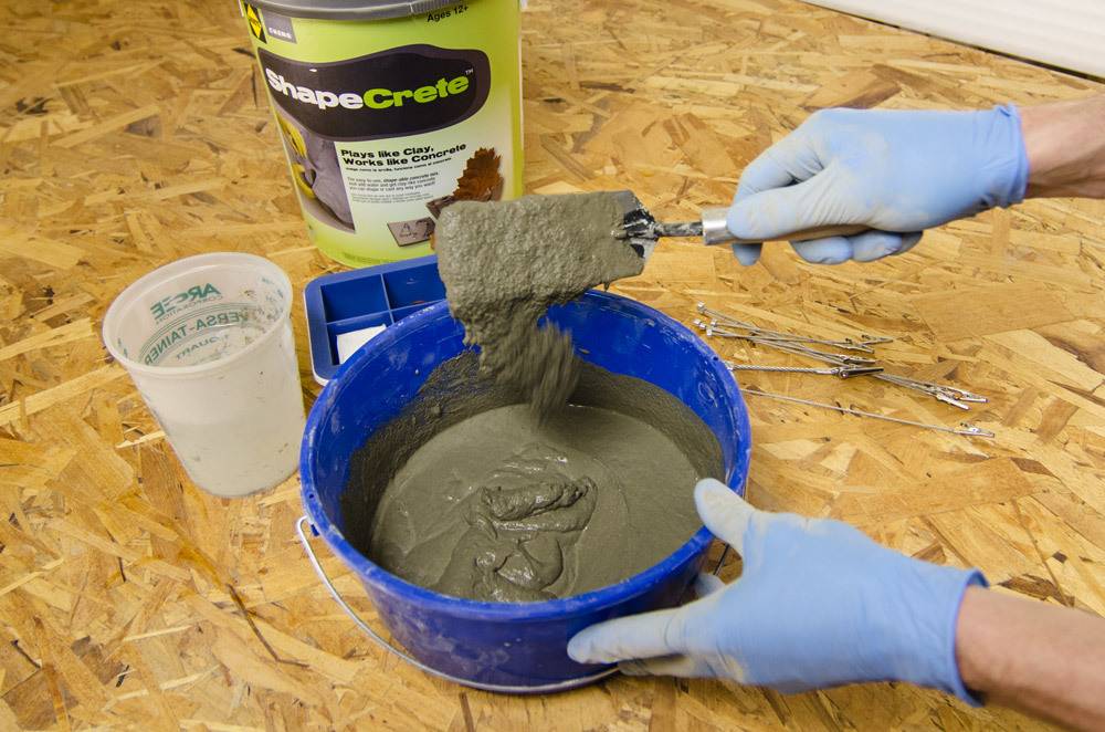 A person with light blue gloves mixes cement in a blue bowl.