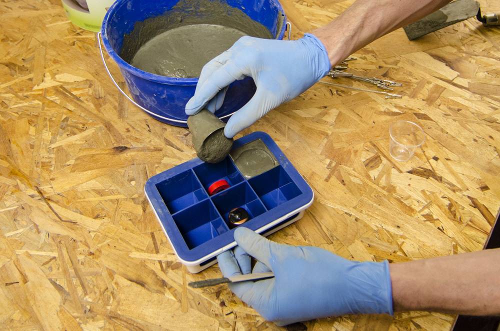 Man wearing blue rubber gloves holding a concrete cube made from a concrete mixing bowl.