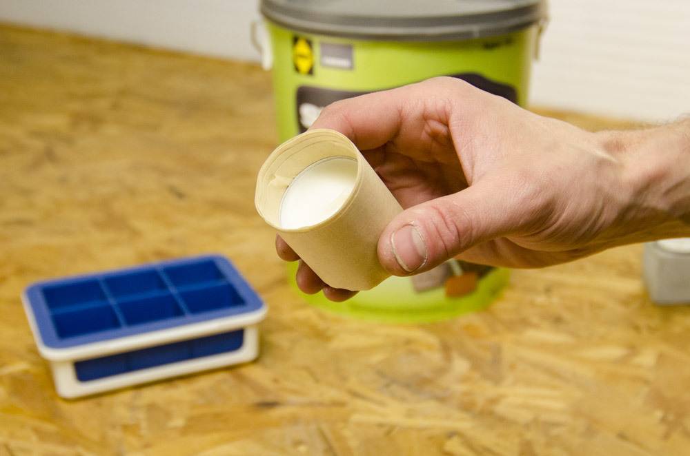Man holding a small container with a white substance in it over a wooden work bench.