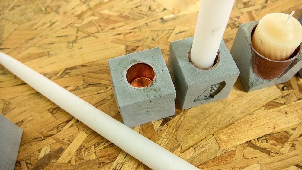 Concrete cube candle holders with candles on a piece of wood.