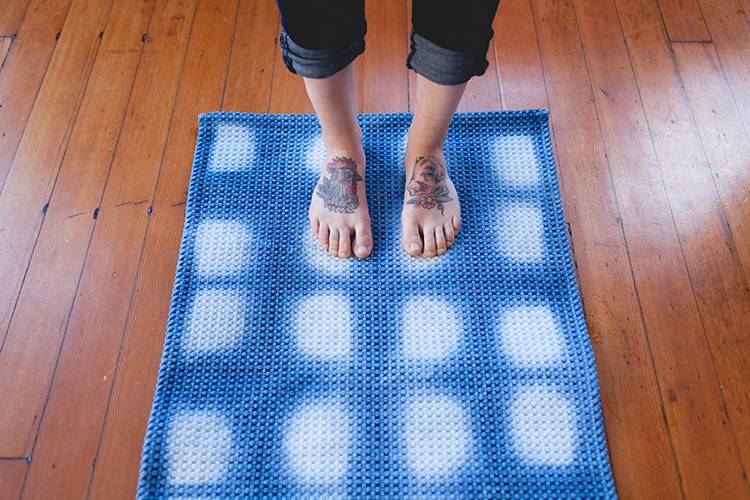 Two tatooed feet standing on a blue and white carpet that is laying on a wood floor.