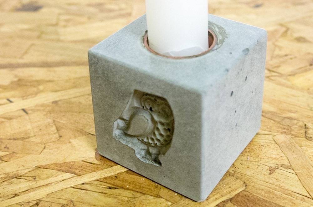 A cubical candle holder with an owl  on it, siting on a wooden surface.