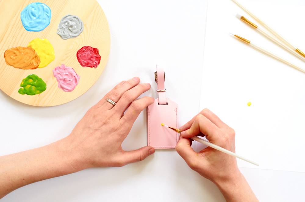 Two hands are painting an object next to paint and brushes.