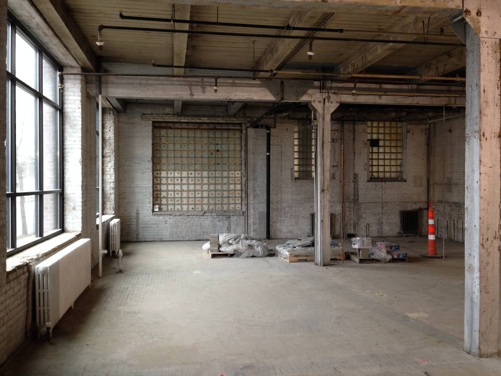 An empty room in an industrial building with  wa largei window is stripped down to the studs.