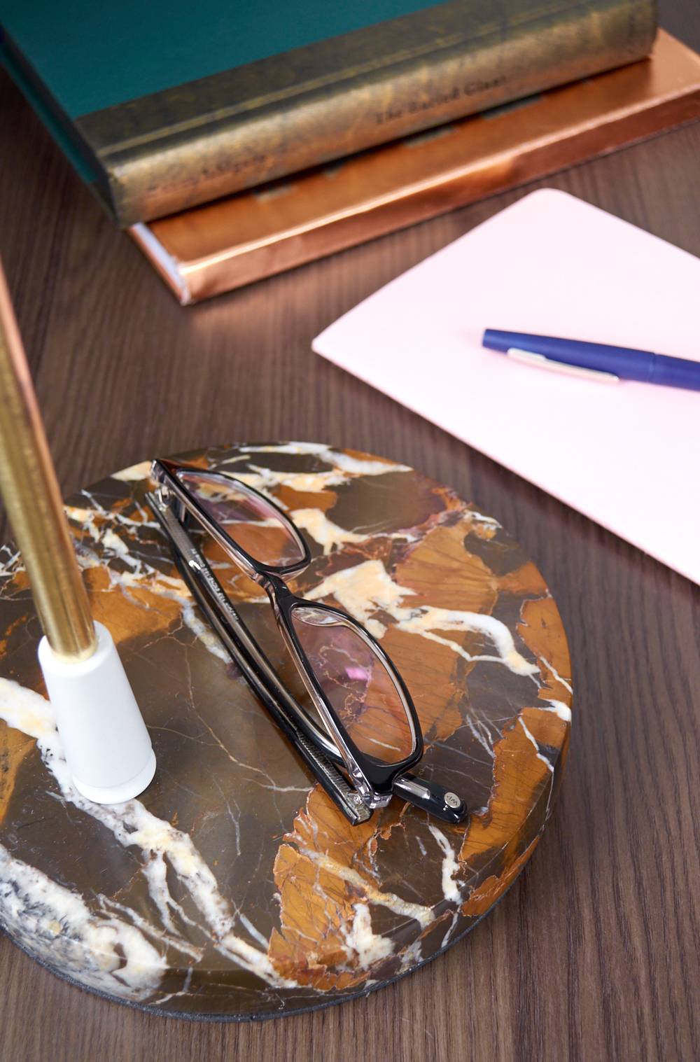 A pair of glasses sits on an object near a paper with a blue ink pen.