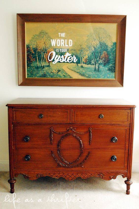 A picture hangs in a wooden frame above a wooden dresser.