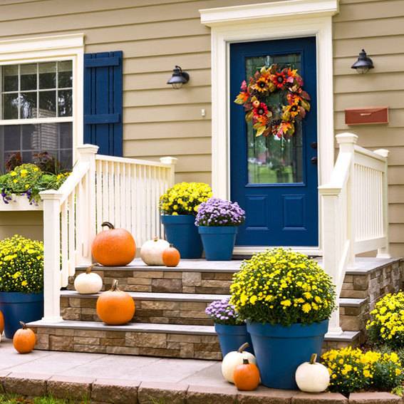 Pumpkins are place on the outer steps of a home along with planted pots.