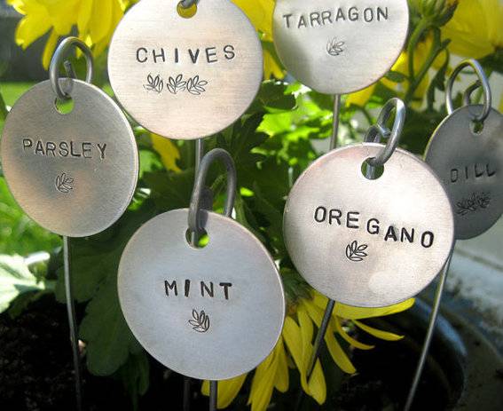 Silver tags with herb names are used to identify the plants in this small herb garden.