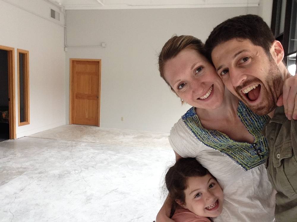 Two adults and a little girl pose in an empty room.
