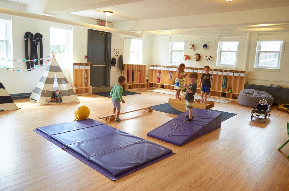 Children are playing on blue mats in a large room.