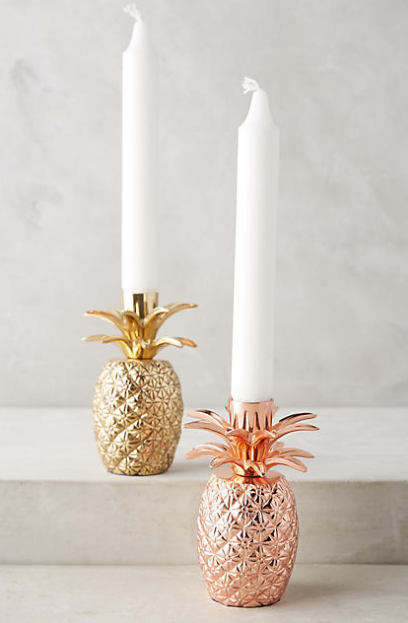 A gold and a peach metalic pineapples as candle holders for tall white candle sticks.