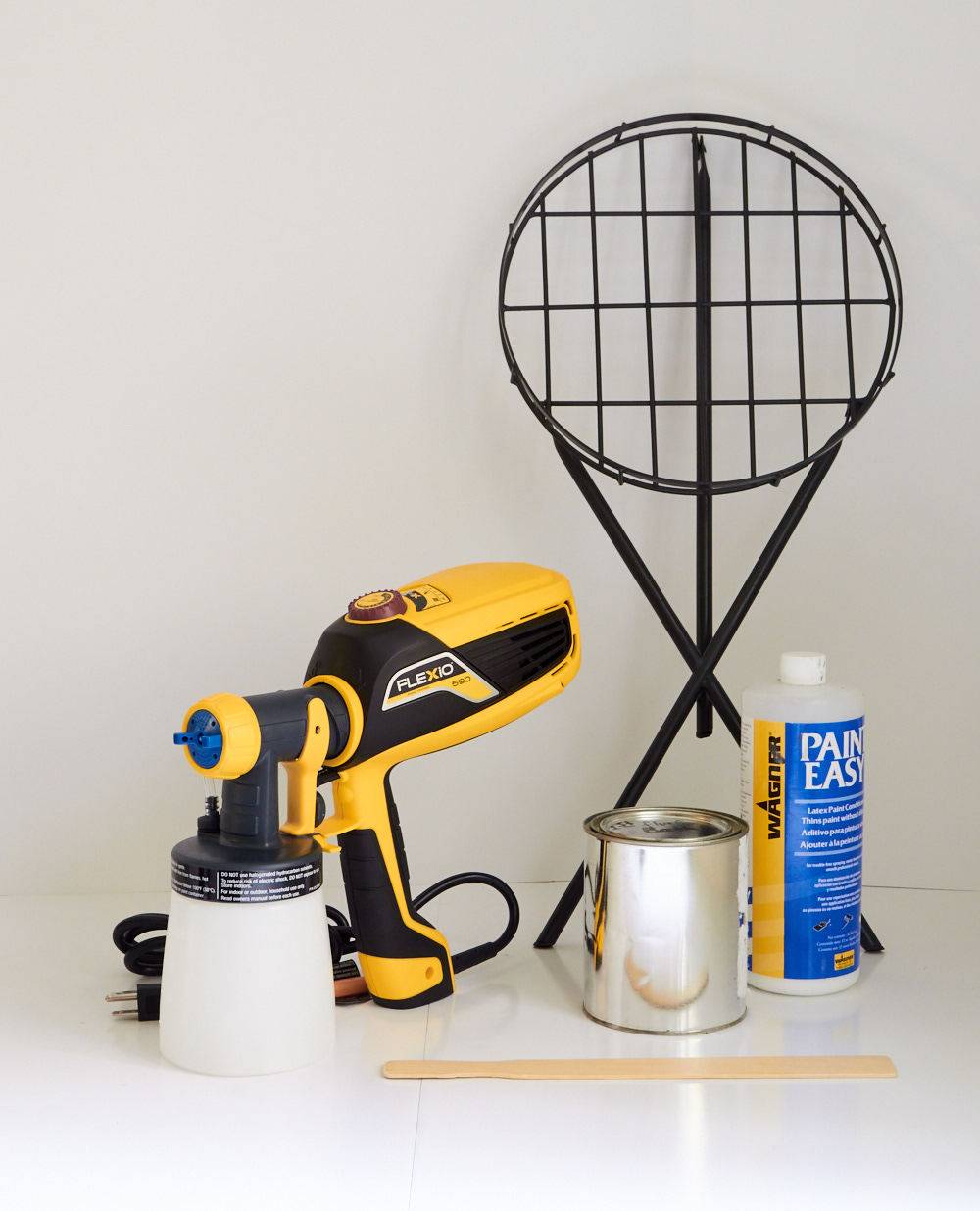 A tennis racket, drill machine, metal box and paint bottle are standing on the floor.