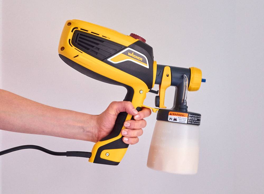 A person is holding a black and yellow machine used for paint.