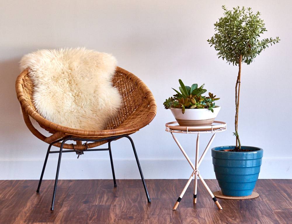 Small wooden chair with a fur blanket on it next to a small wooden table and plant in a blue pot.