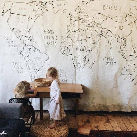 Kids playing standing near a beautiful big map placed on wall .