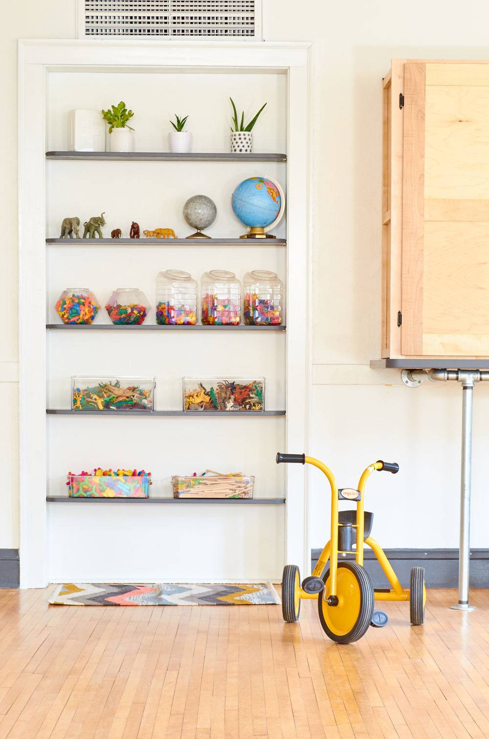A yellow and grey trike sits on the wooden floor near a bookshelf.