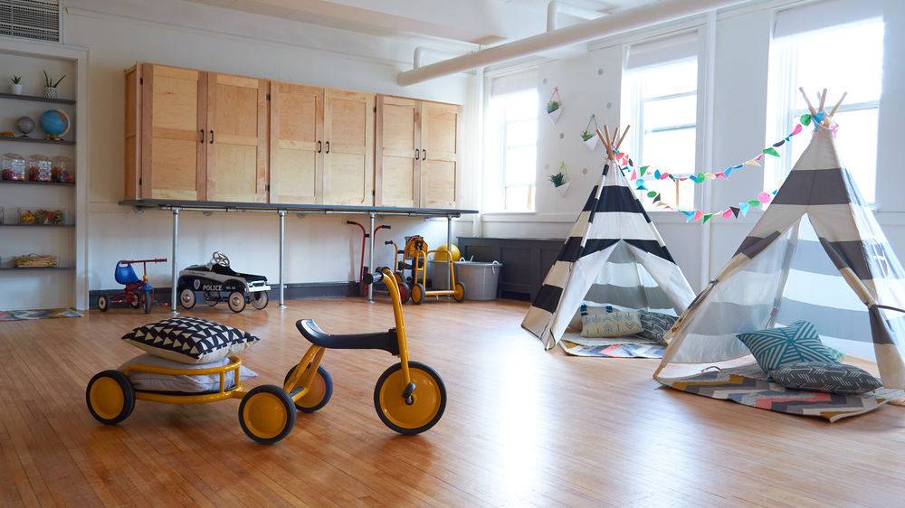 A nursery school classroom with 2 tents, a tricycle that pulls a wagon and other riding toys for children.