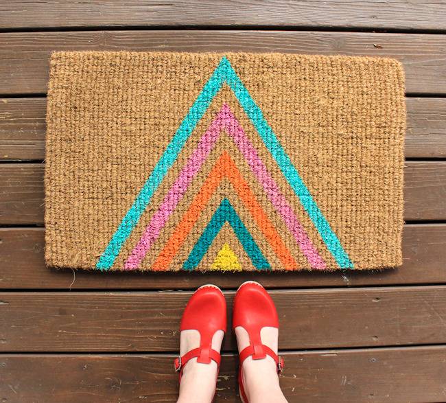 A person in red shoes standing on a wooden porch in front of a colorful welcome mat.
