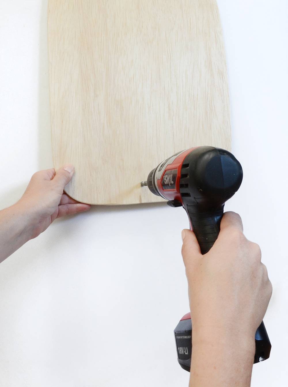 A hand holding a piece of light colored wood while another hand is using a hand drill.