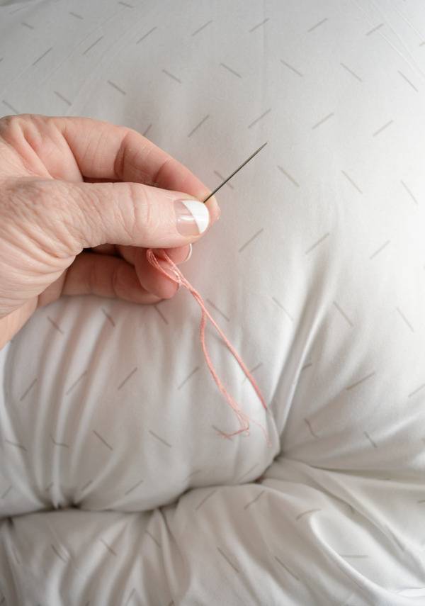 A person is using a needle and thread to sew a pet bed.