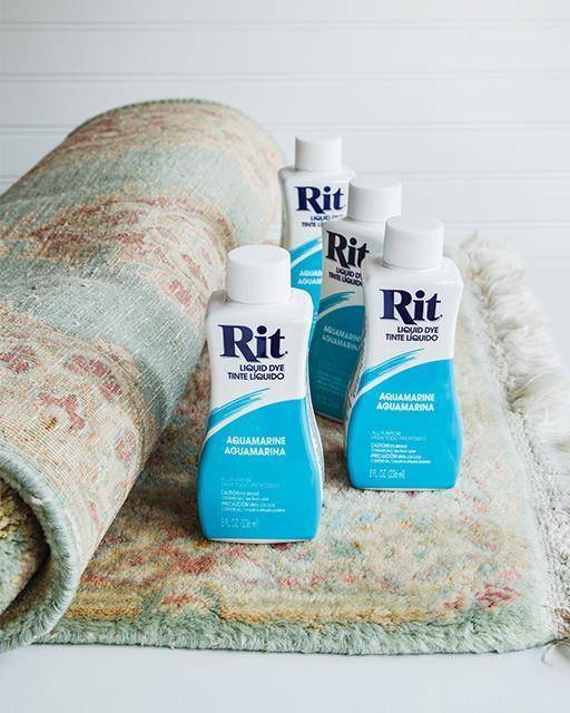 Four bottles of Rit dye sit on top of a partially rolled rug.