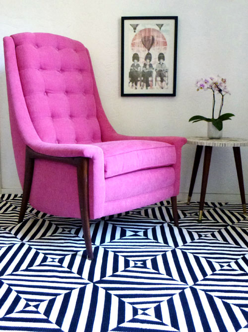 A pink chair sits on black and white striped floor.